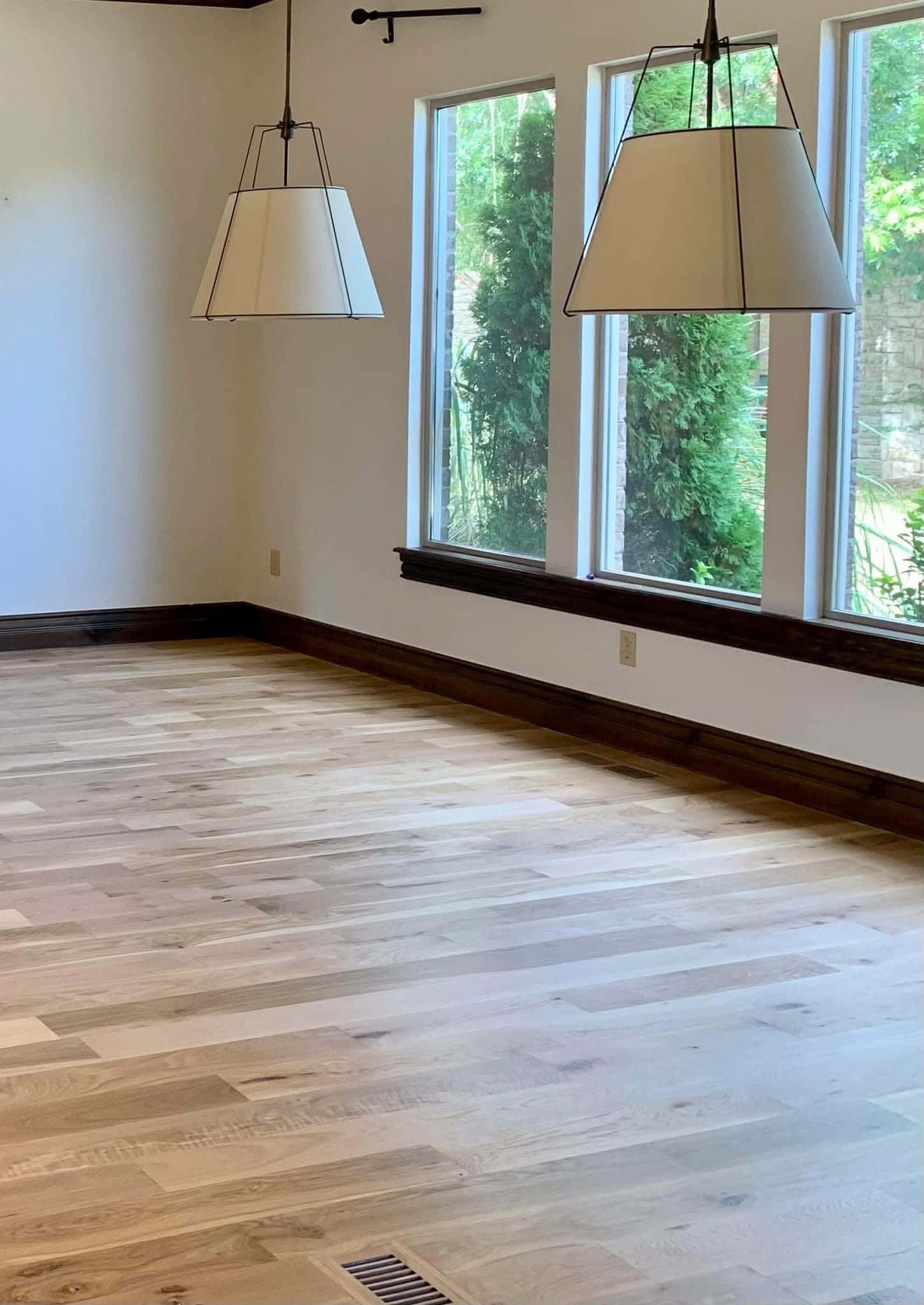 Signature natural wide-plank hardwood flooring installation with large sunlit windows.